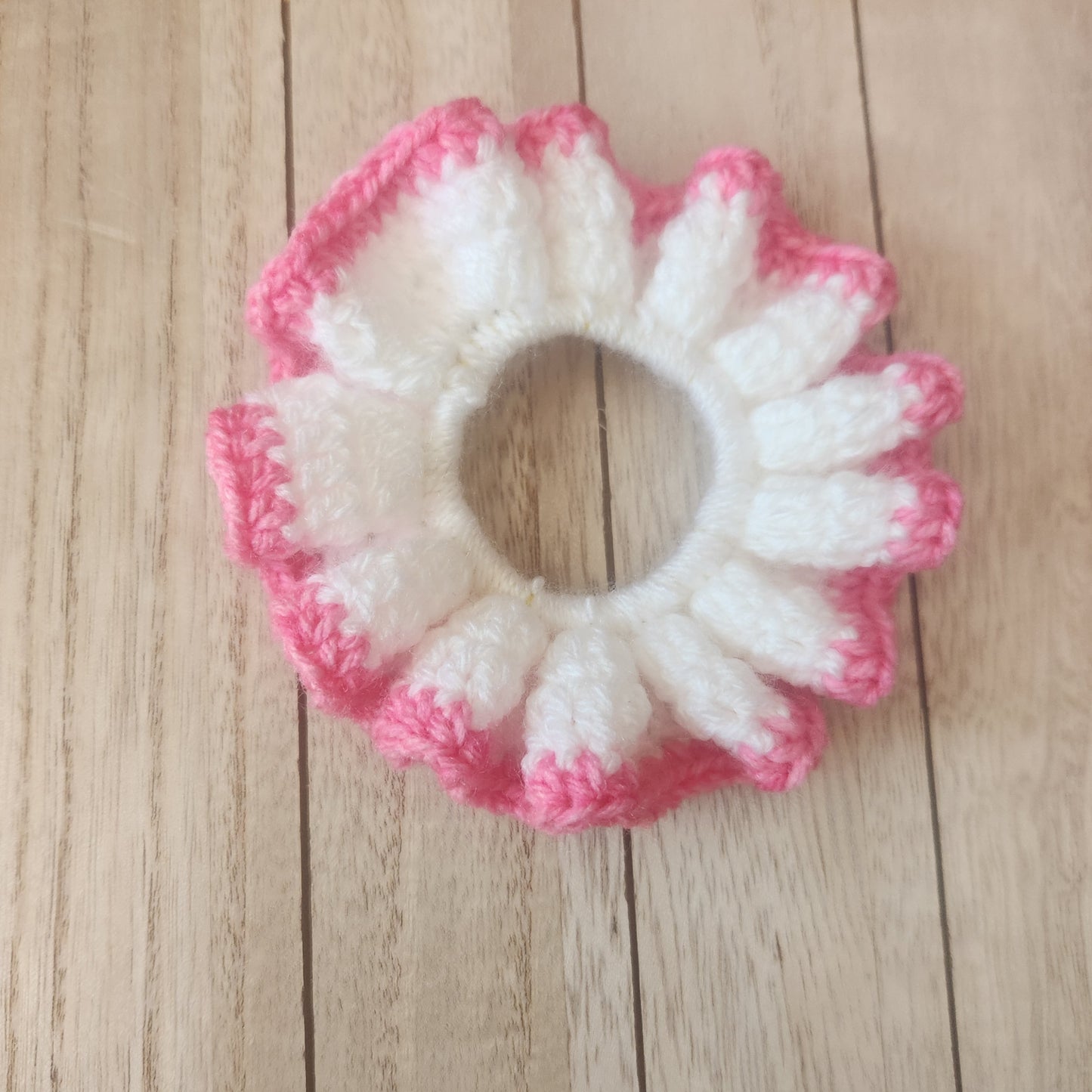 Crocheted flower-shaped item with pink and white colors on a wooden surface