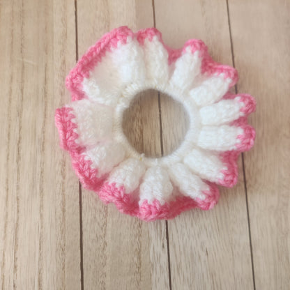 Crocheted flower-shaped item with pink and white colors on a wooden surface